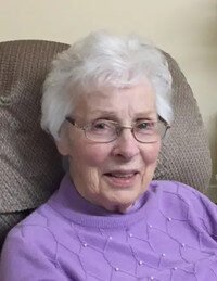 Smiling elderly woman with glasses and white hair.