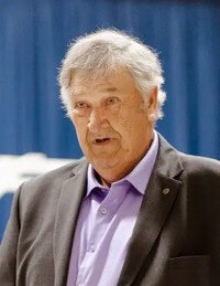 Elderly man in suit speaking at event.