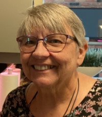 Smiling person with short gray hair and glasses.