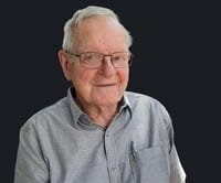 Smiling elderly man with glasses and gray shirt.