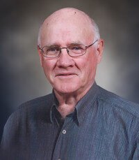 Elderly man wearing glasses, gray shirt, smiling.